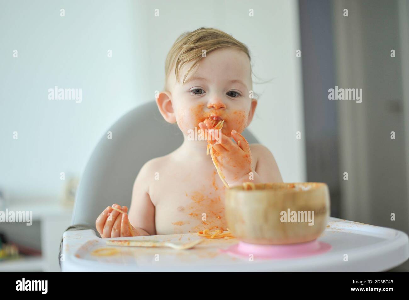 Baby eating pasta sitting on high chair Stock Photo Alamy