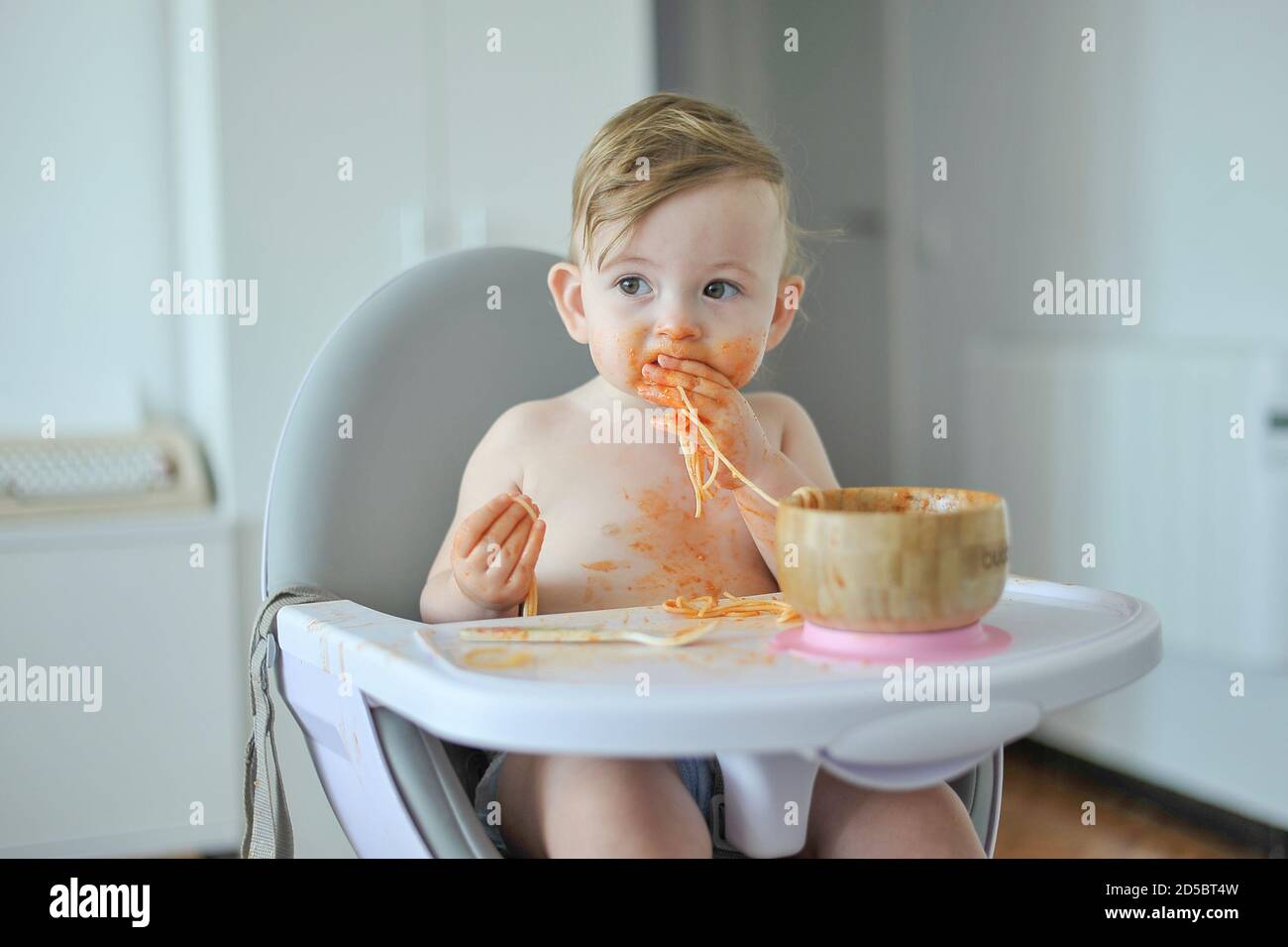 Baby eating pasta sitting on high chair Stock Photo