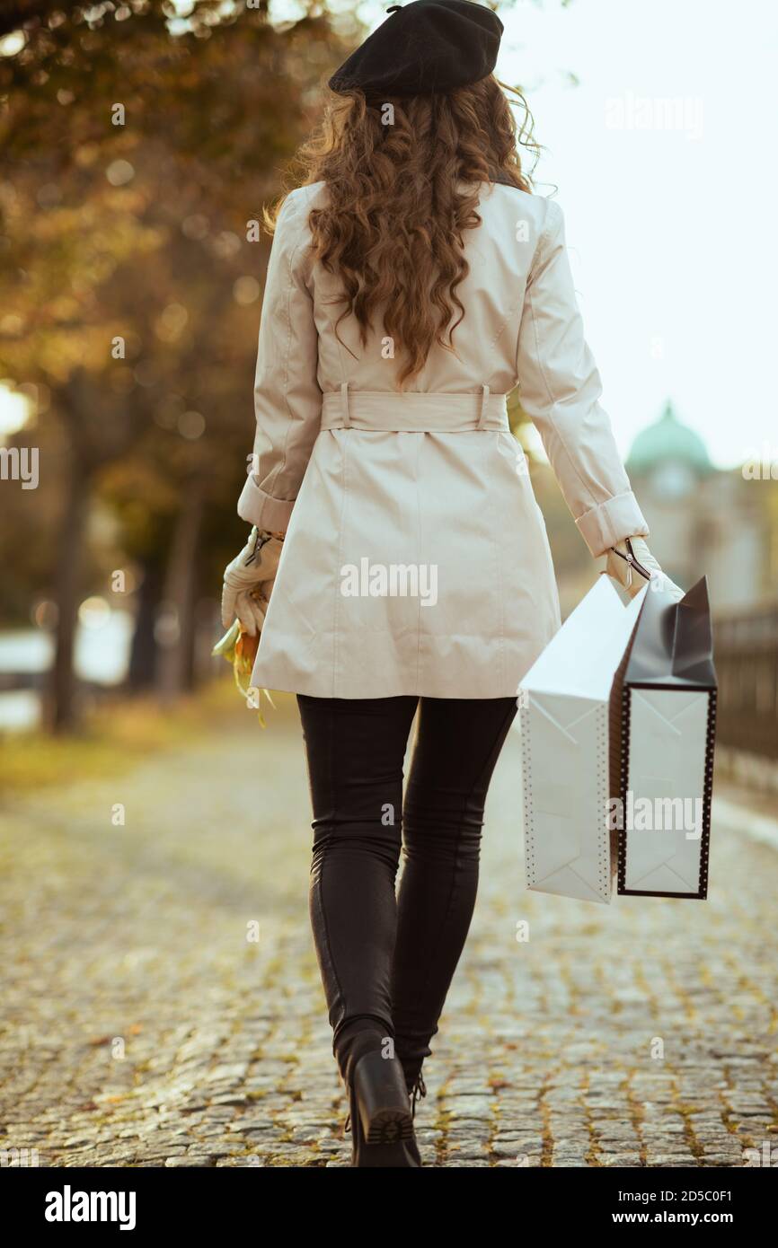 Hello october. Seen from behind young female in beige trench coat with  shopping bags outdoors on the city street in autumn Stock Photo - Alamy
