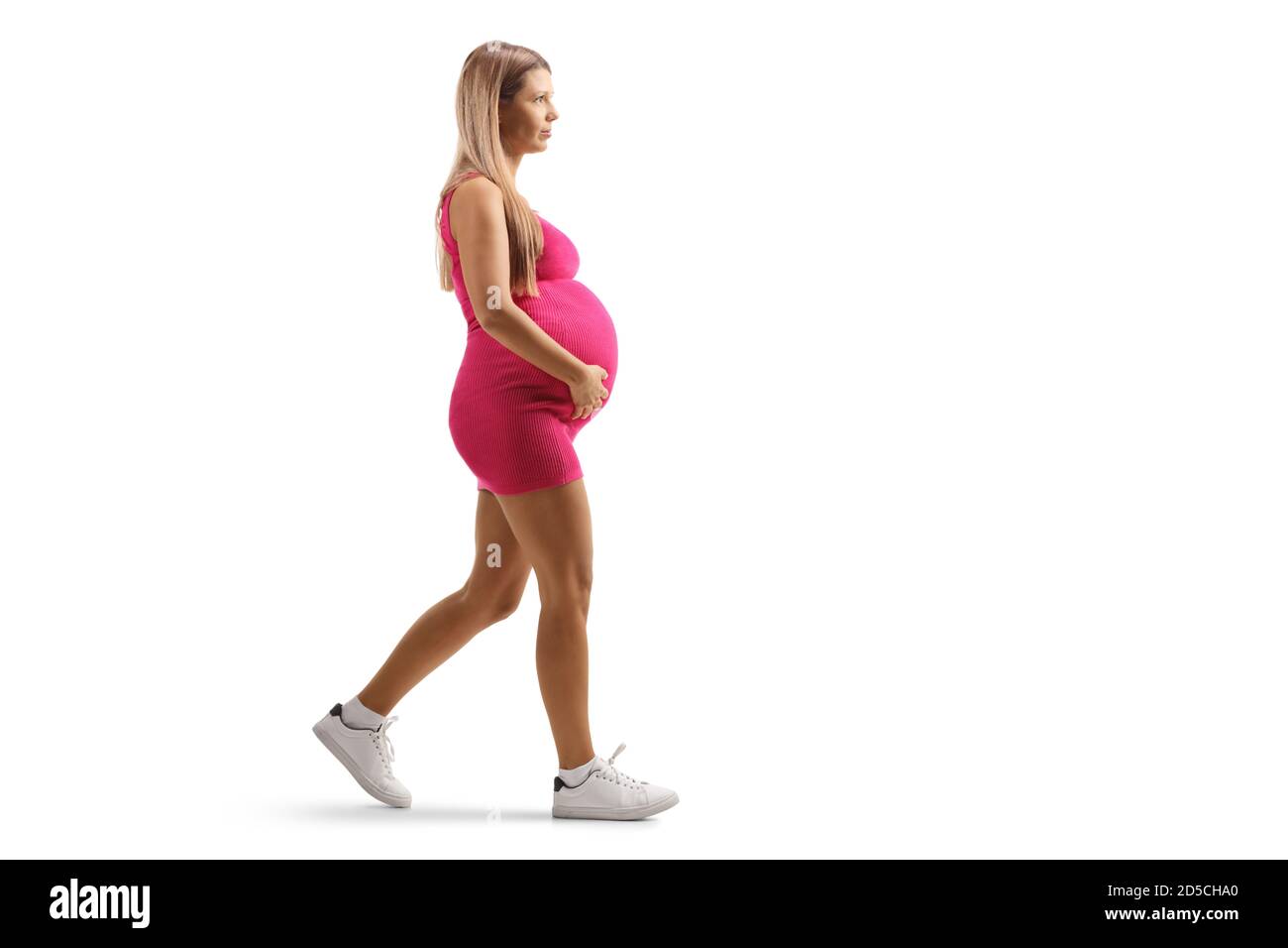 Full length profile shot of a young pregnant woman in a pink dress walking isolated on white background Stock Photo