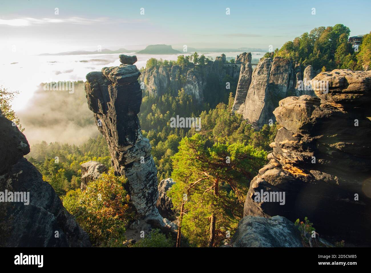 Picuresque  viev over the wehlground to the Bastei bridge with fog in the valley during the sunrise. The distinctive Wehl needle in the foreground. Stock Photo
