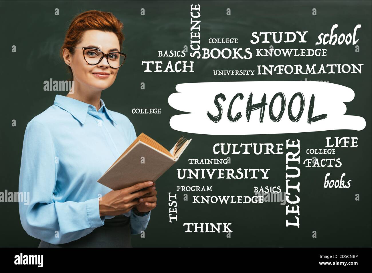 teacher in eyeglasses holding book near chalkboard with lettering in ...