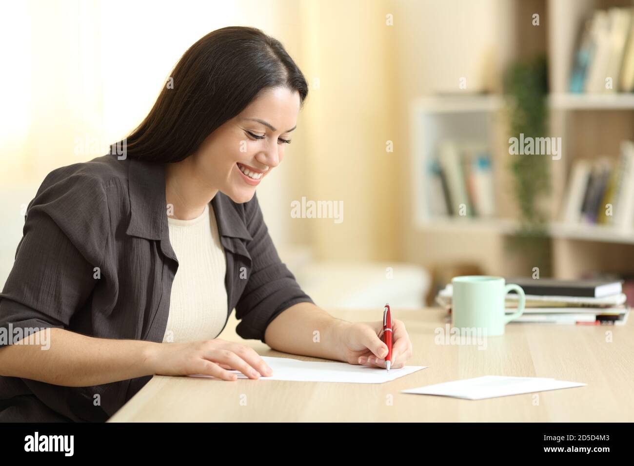 Happy woman writing letter on a table at home with a warm light Stock Photo