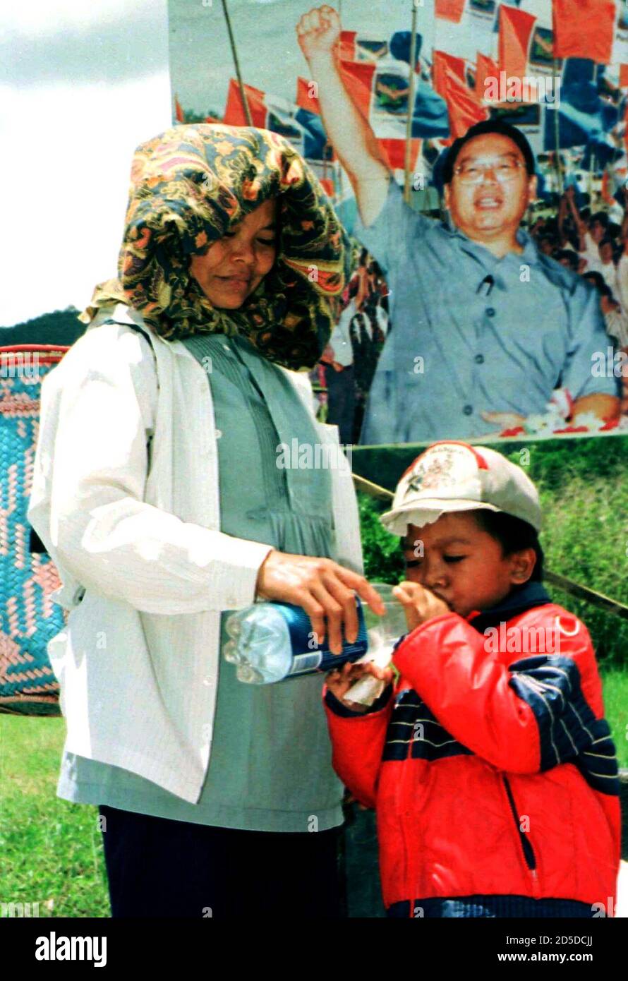 A boy drinks water given to him by his mother under a huge 