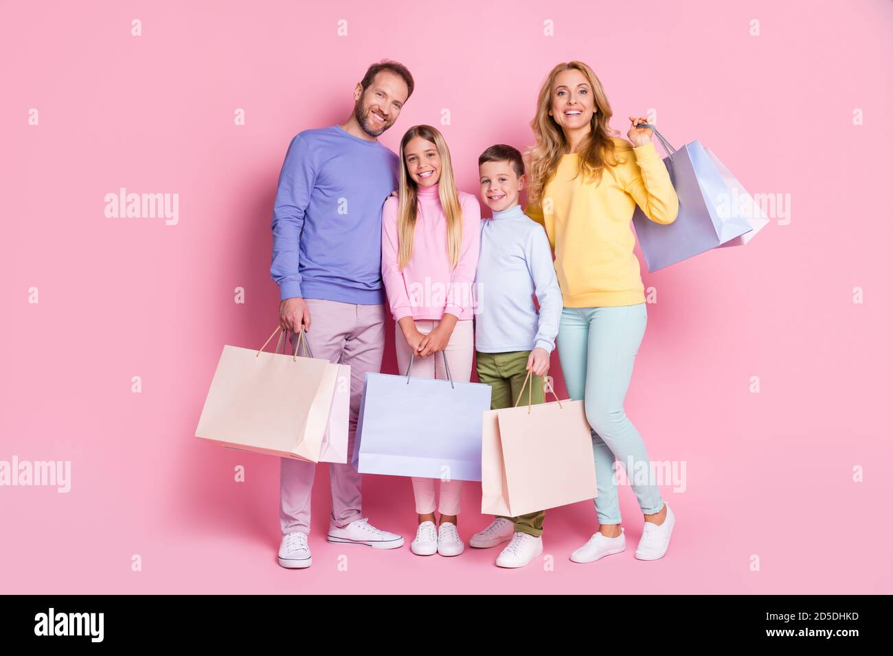 Full size photo of positive family daddy mommy small kids boy girl hold shopping bags isolated over pastel color background Stock Photo