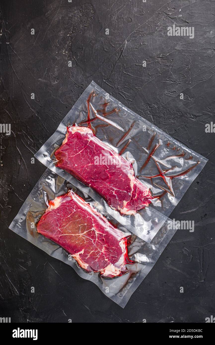 Rump steak in vacuum sealed bag on black textured background, side view