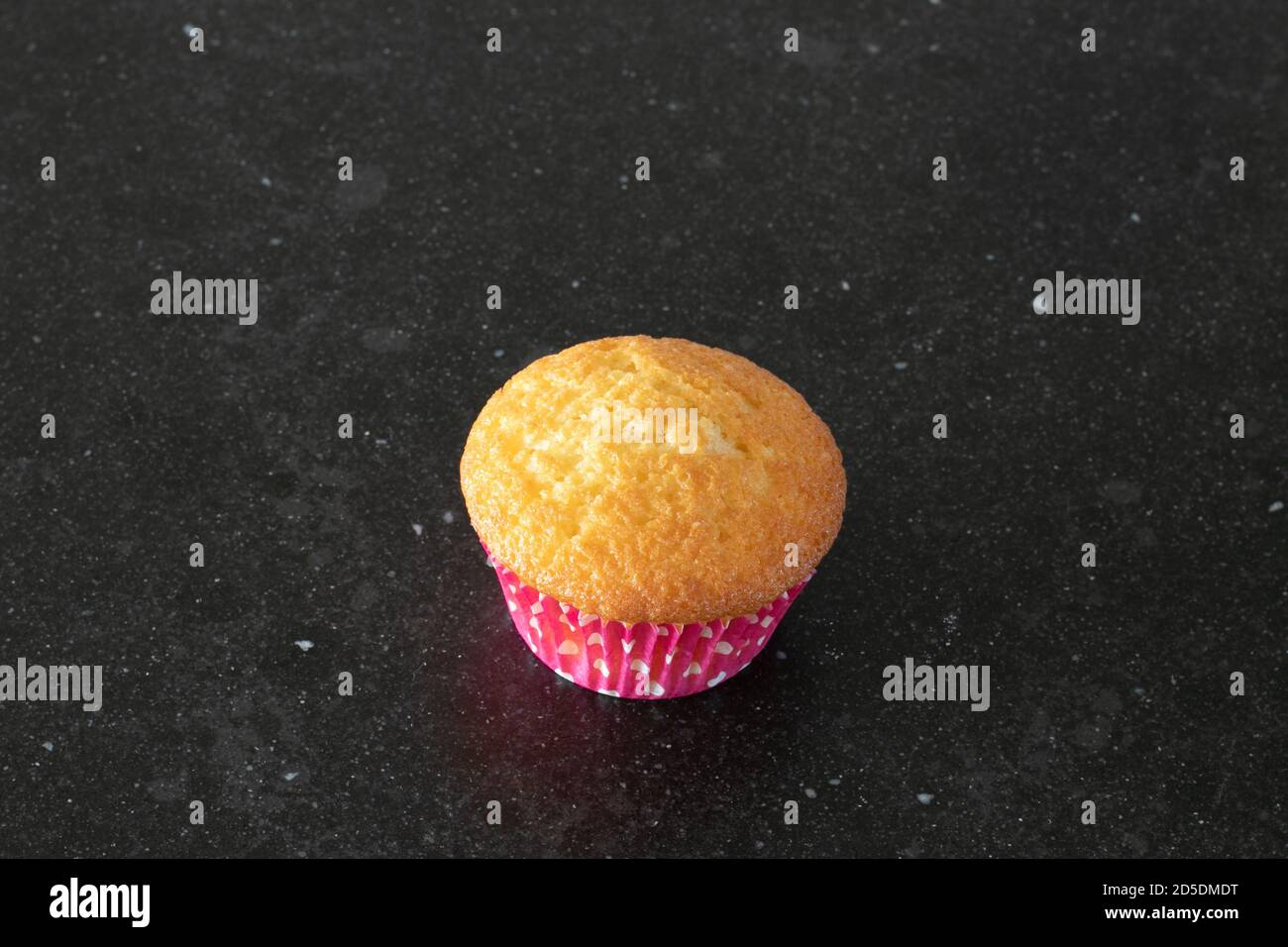One home baked cupcake in a dark background, marble table top, pink with dots Stock Photo