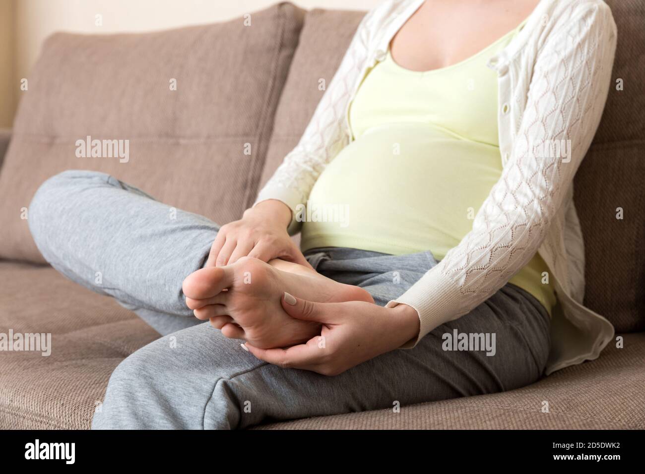 Leg cramps during pregnancy. Closeup of hands massaging swollen foot