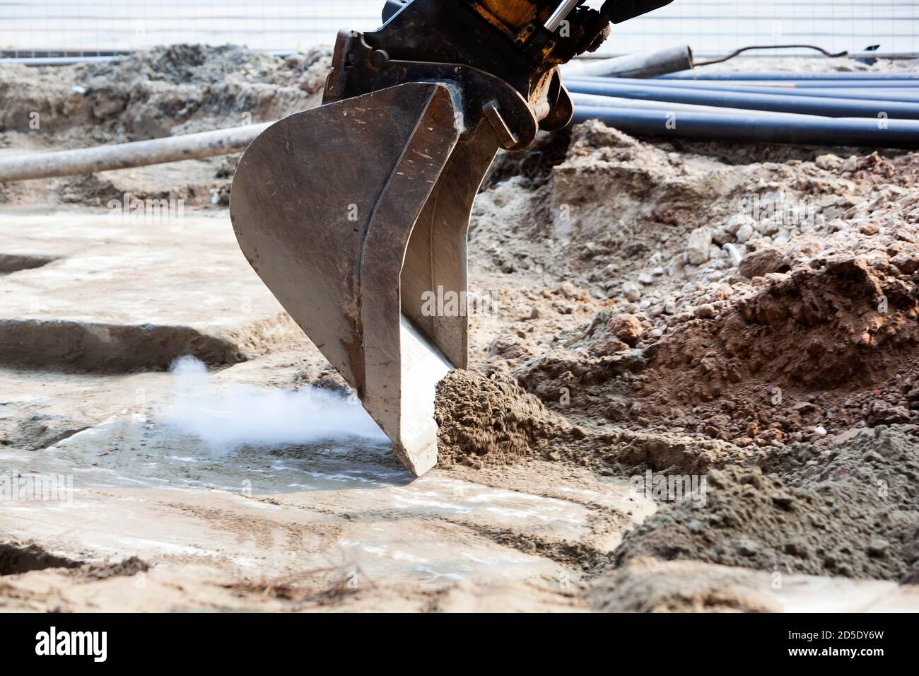 Closeup of an excavator producing smoke while scraping sand from concrete on an construction site Stock Photo