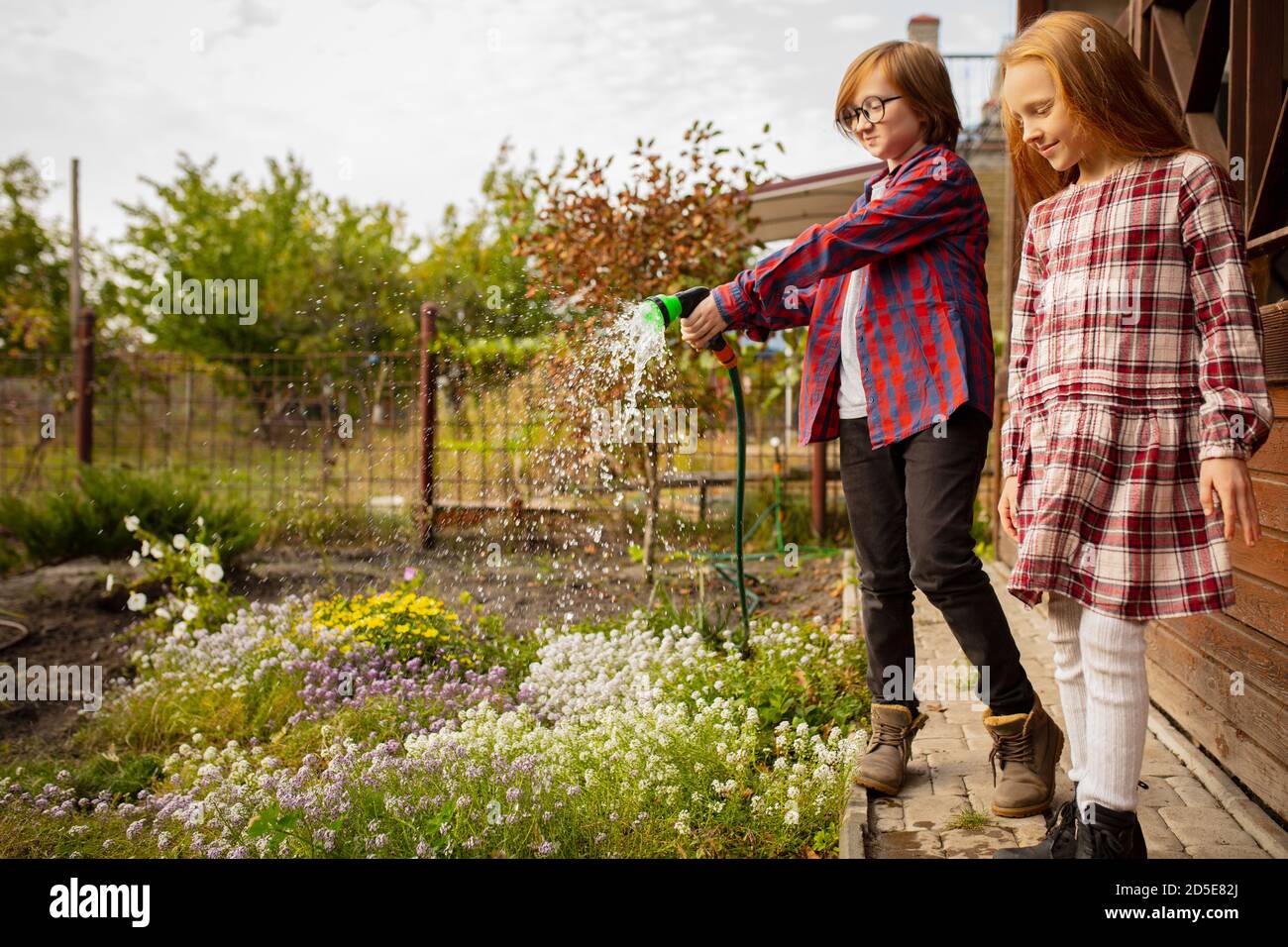 Farmers. Happy brother and sister watering plants in a garden outdoors
