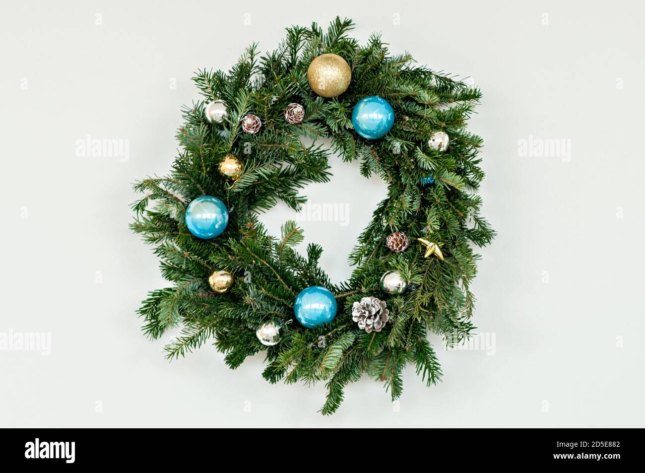 Green festive wreath made of fresh live spruce, decorated with New Year's toys, garlands. Christmas home decoration. Hanging over a fireplace Stock Photo