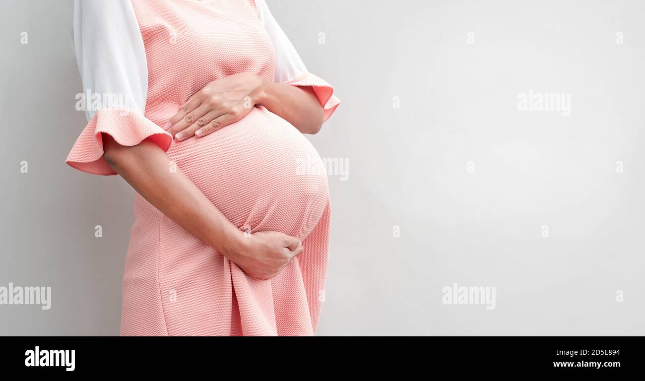 Pregnant woman in dress holds hands on belly on a white background , copy space Stock Photo