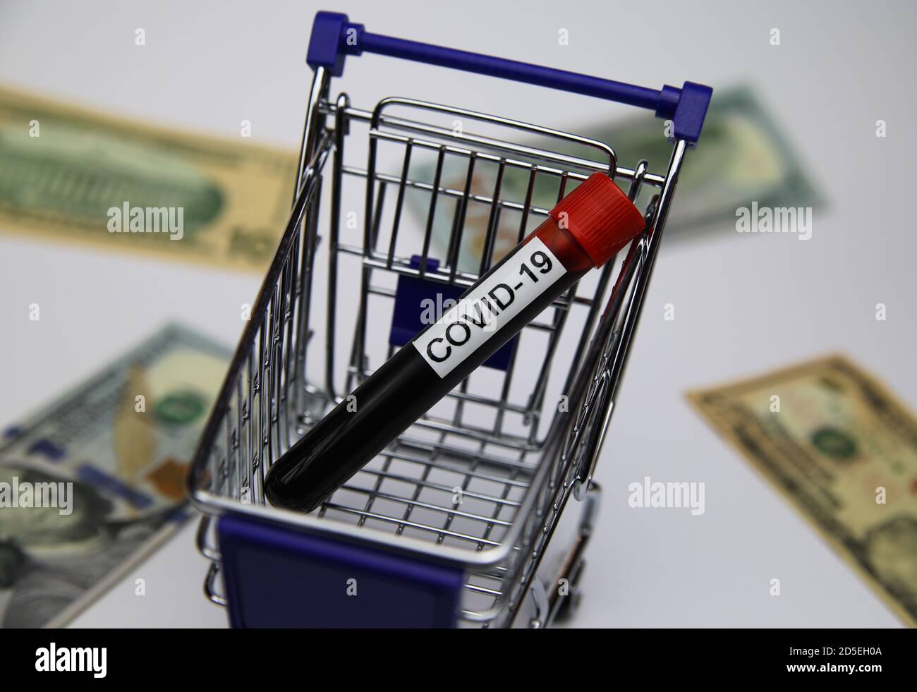 View on modell of shopping cart with covid-19 blood sample tube and us dollar bills background  -consumer behaviour and retail  trade during corona cr Stock Photo