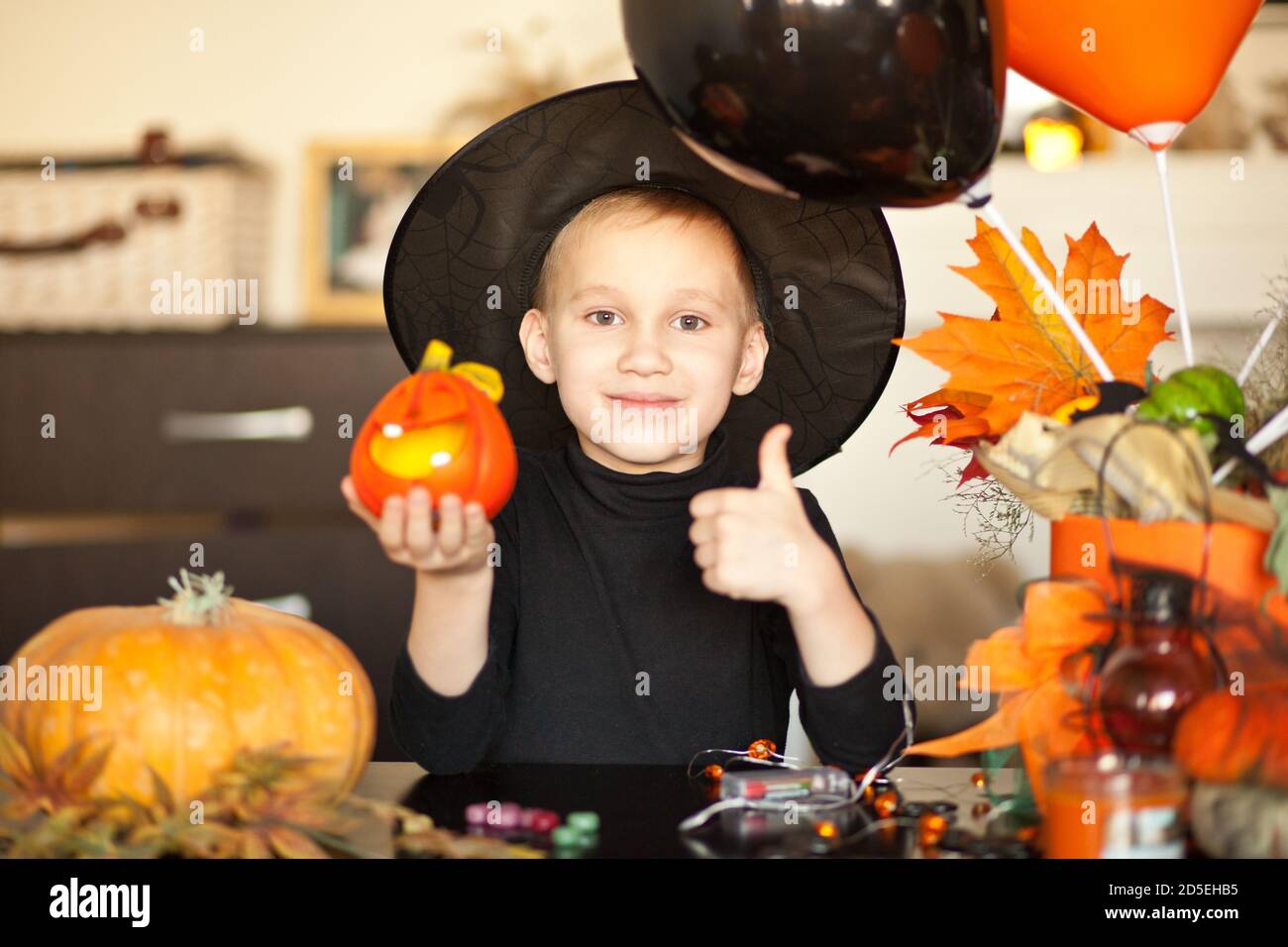 funny kid boy in witch costume for Halloween with pumpkin Jack in a hands. Stock Photo