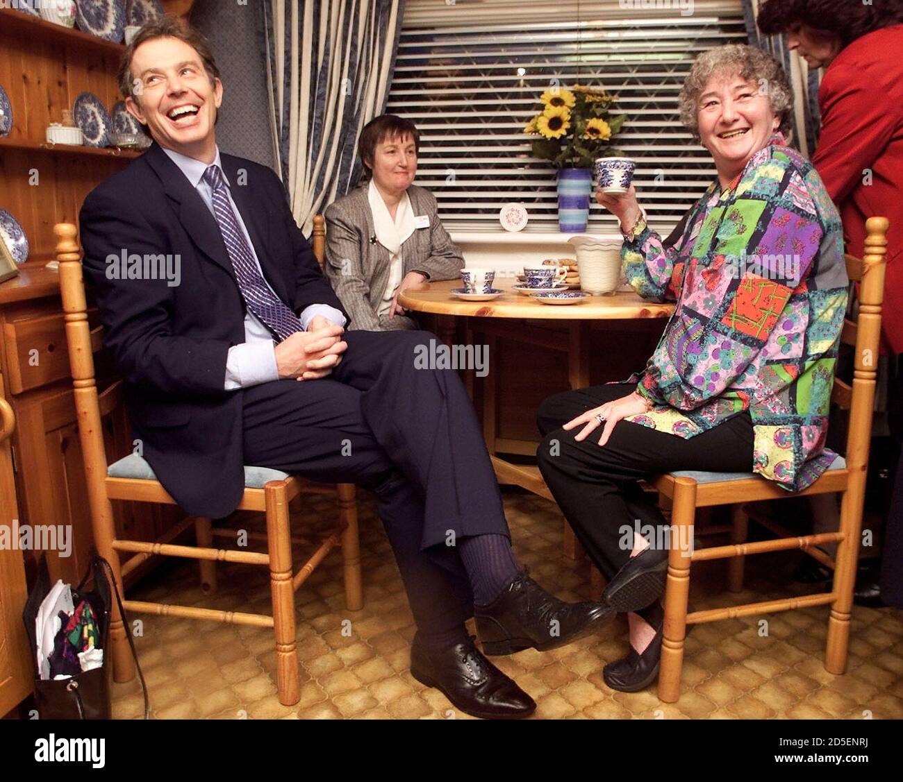 Britain's Prime Minister Tony Blair (L) smiles as he drinks tea with local residents Maggie Warburton (R) and Barbara Taylor during a visit to a housing estate in Manchester December 6. Blair has said that his government policies were starting to tackle Britain's economic blackspots, narrowing the divide betweenthe rich south and the poorer north.  DC/PS Stock Photo
