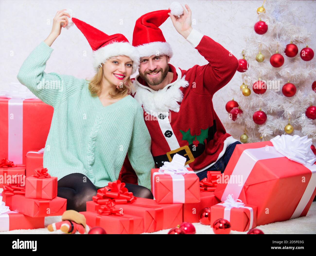 It is easy to spread happiness around. Happy family celebrate christmas. Christmas gift concept. Couple wear hats as santa claus christmas tree background. Couple in love enjoy christmas celebration. Stock Photo
