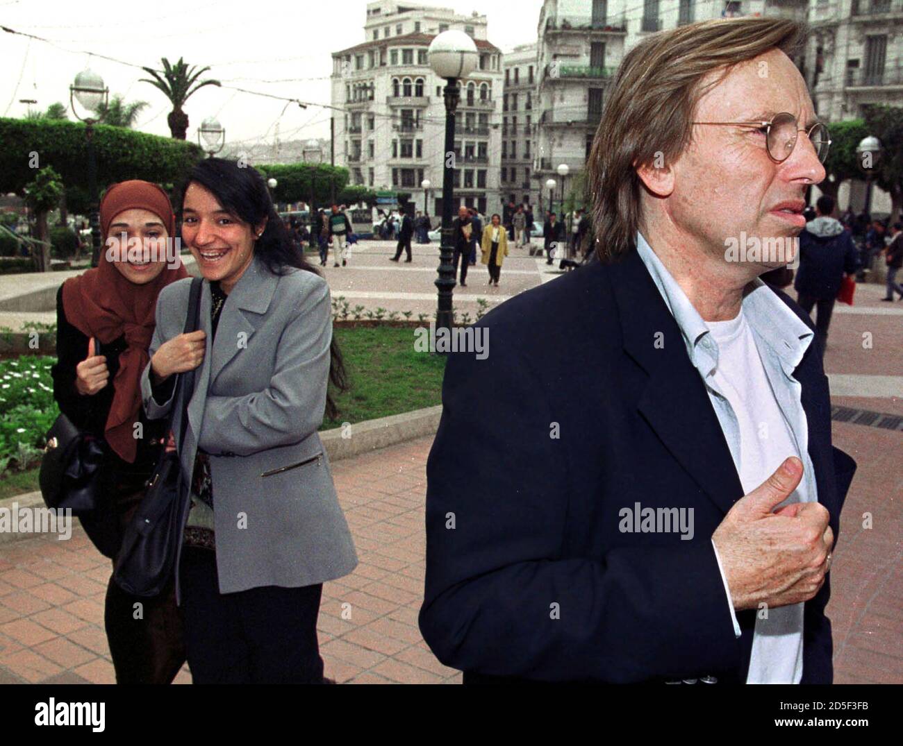 Two Algerian girls walk near French director Alexandre Arcady (R) in  Algiers April 8. Arcady is in Algiers for the first screening of their film  "La-bas, mon pays" (There, my country Stock