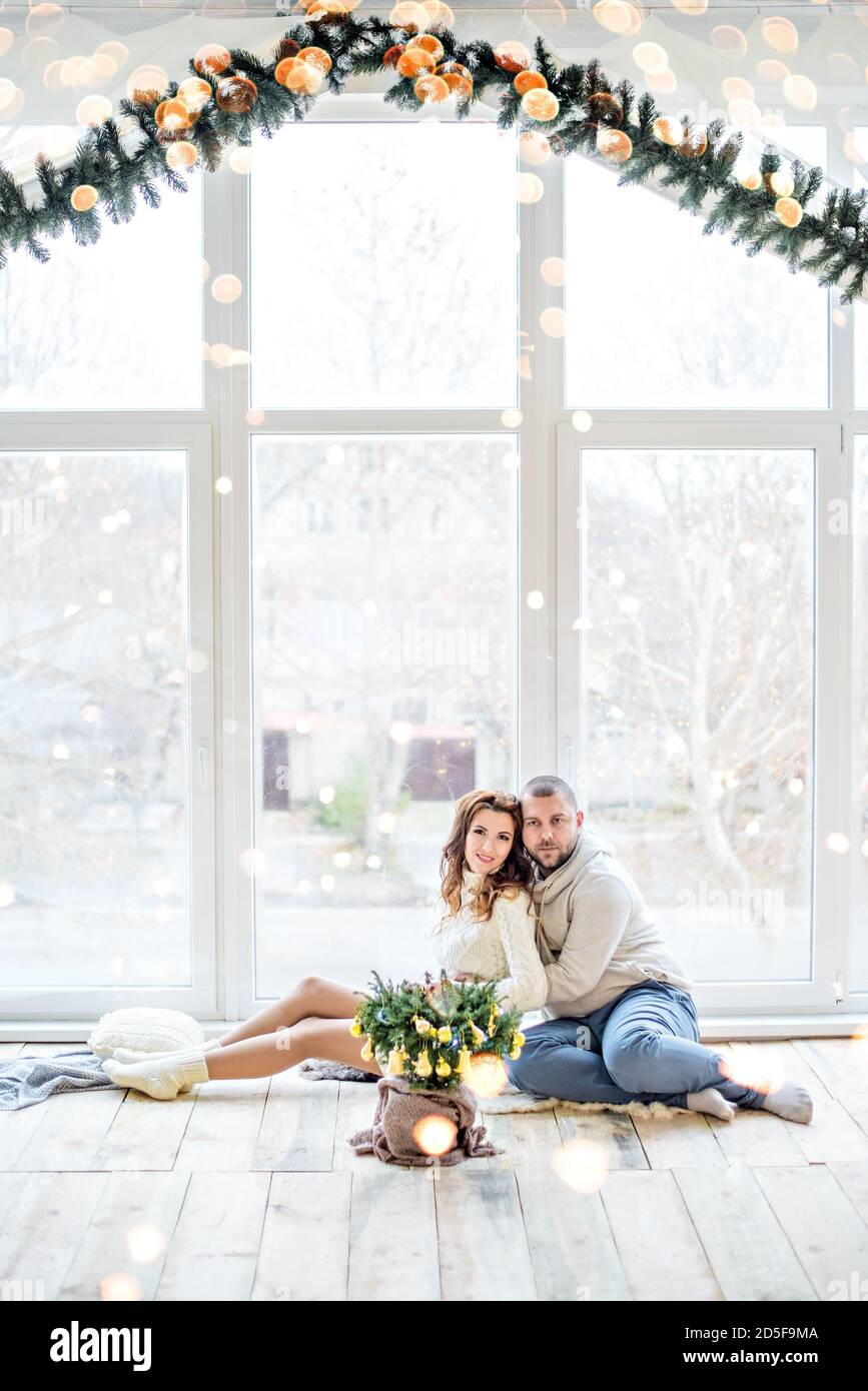 Happy couple in love sits on the wooden floor by the panoramic window ...