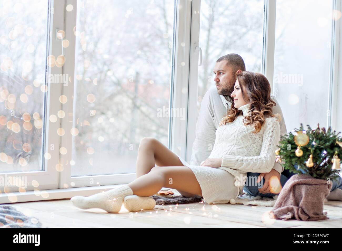 Happy couple in love sits on the wooden floor by the panoramic window ...