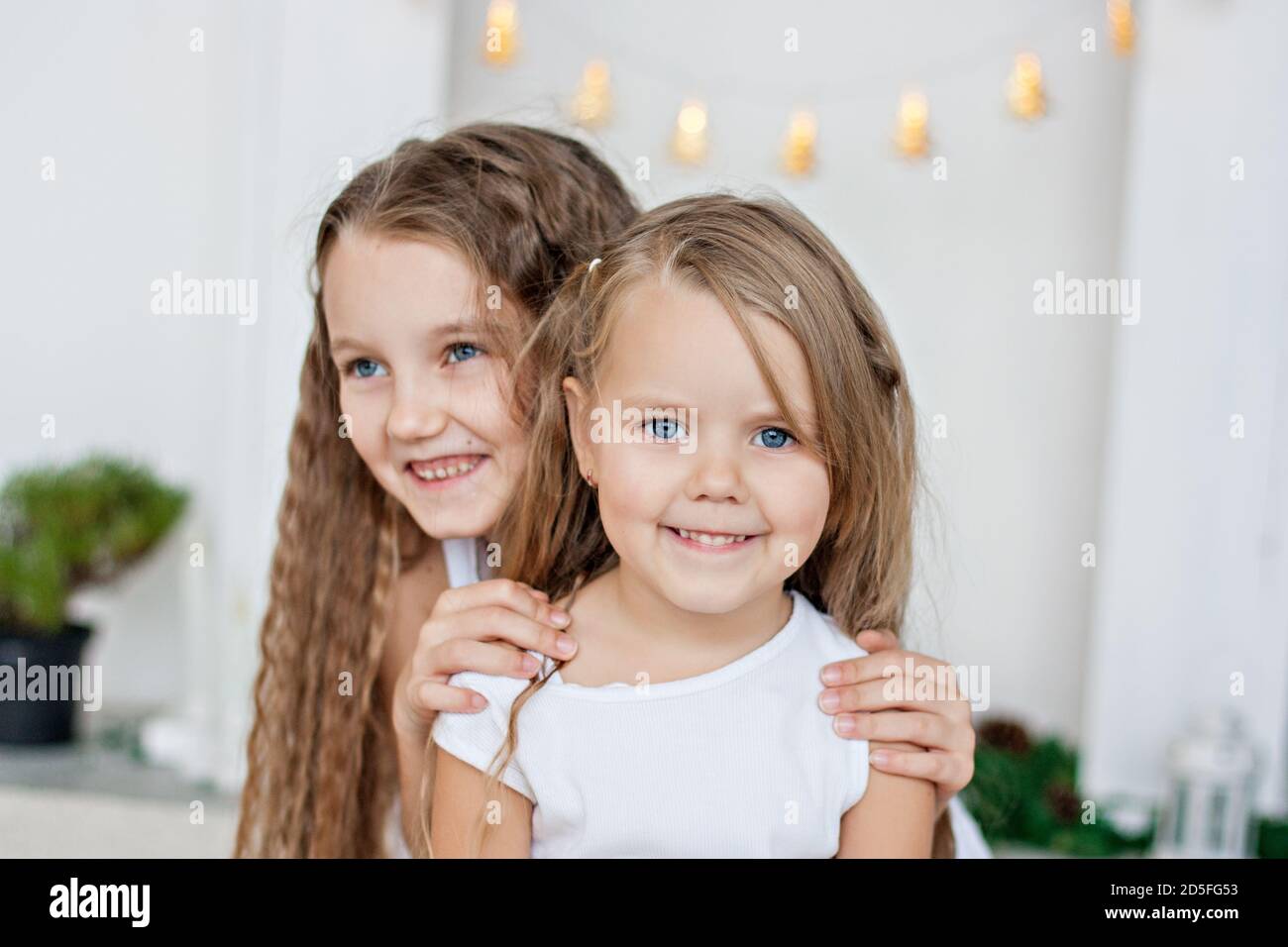 Two little blonde girls in white dresses are playing by the fireplace ...