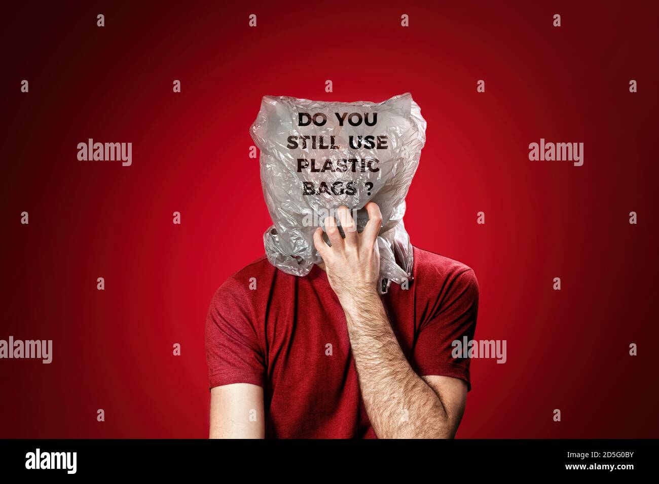 The man reaches for his mouth, feeling suffocated in a plastic bag. Red background. Concept of pollution and environmental protection. Stock Photo