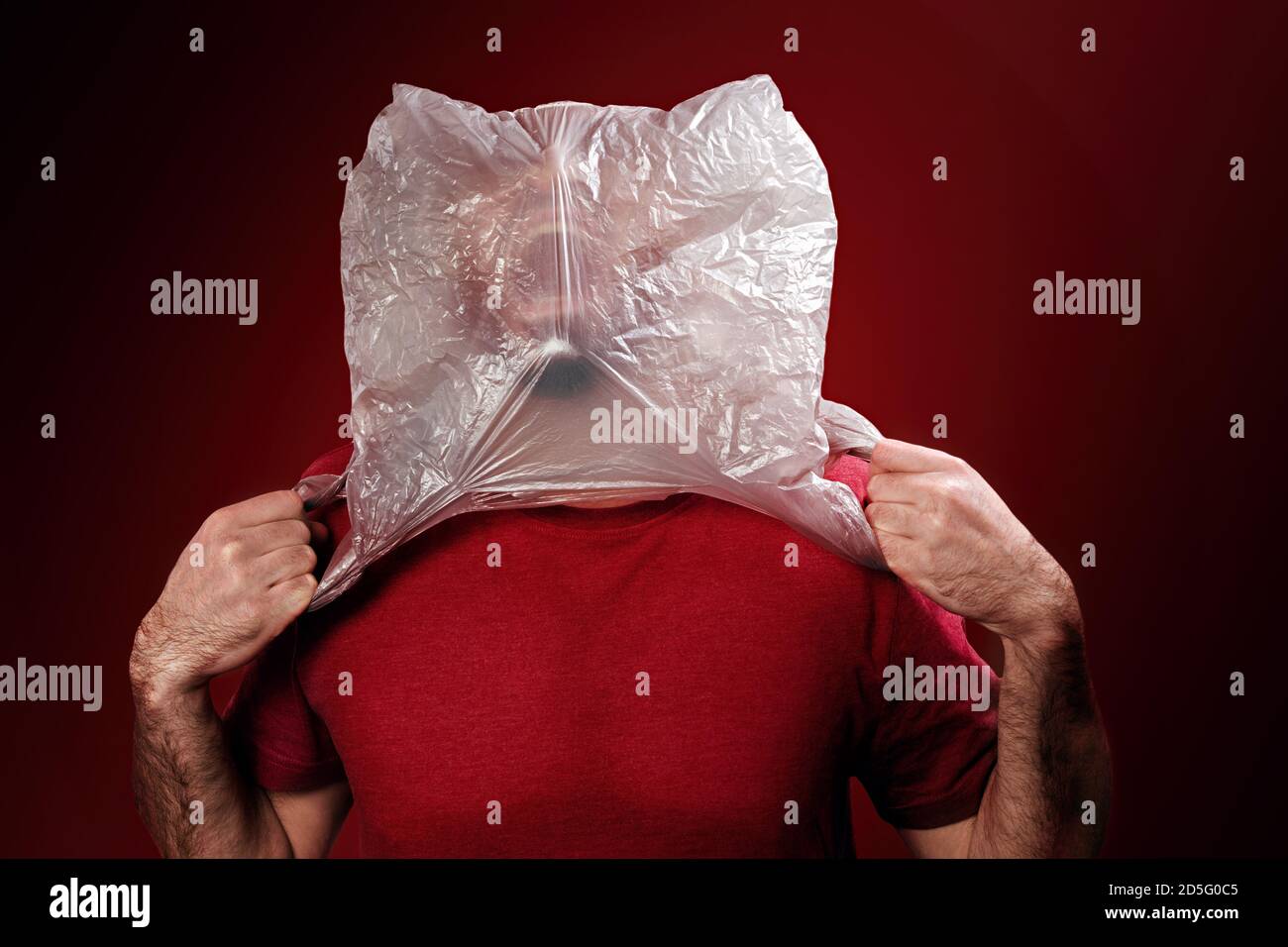 The man rips off the plastic bag from his head, suffocating. Red background. Copy space. Concept of pollution and environmental protection. Stock Photo