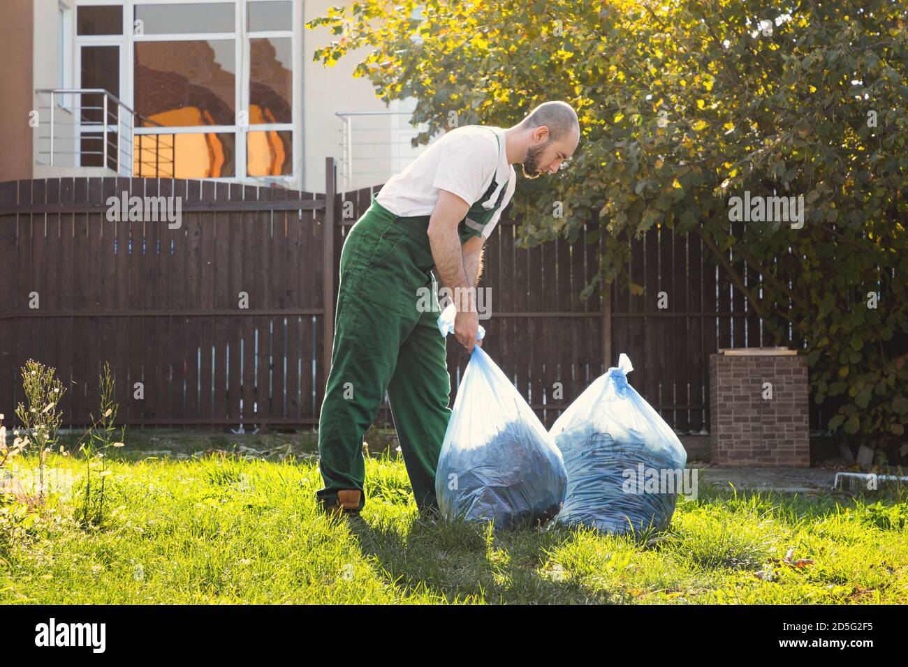 Gardener picks up bags of leaves to remove debris from the territory. Green uniform. Stock Photo