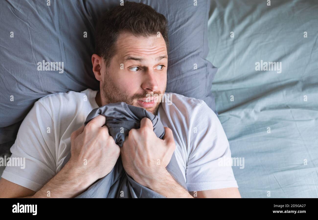 Scared Man Lying In Bed At Home At Night Stock Photo