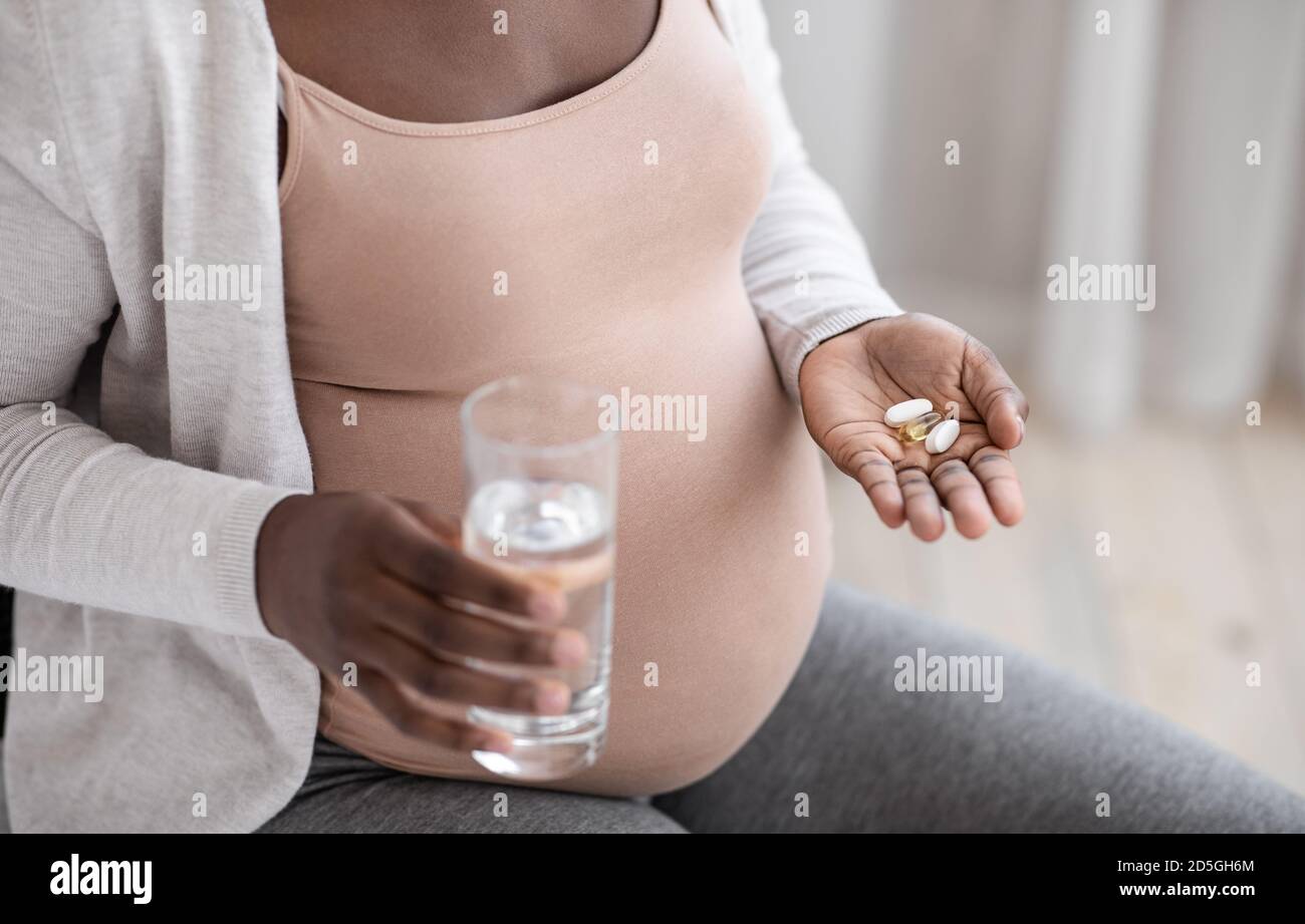Prenatal Vitamins And Supplements. Unrecognizable black pregnant woman taking pills and water Stock Photo