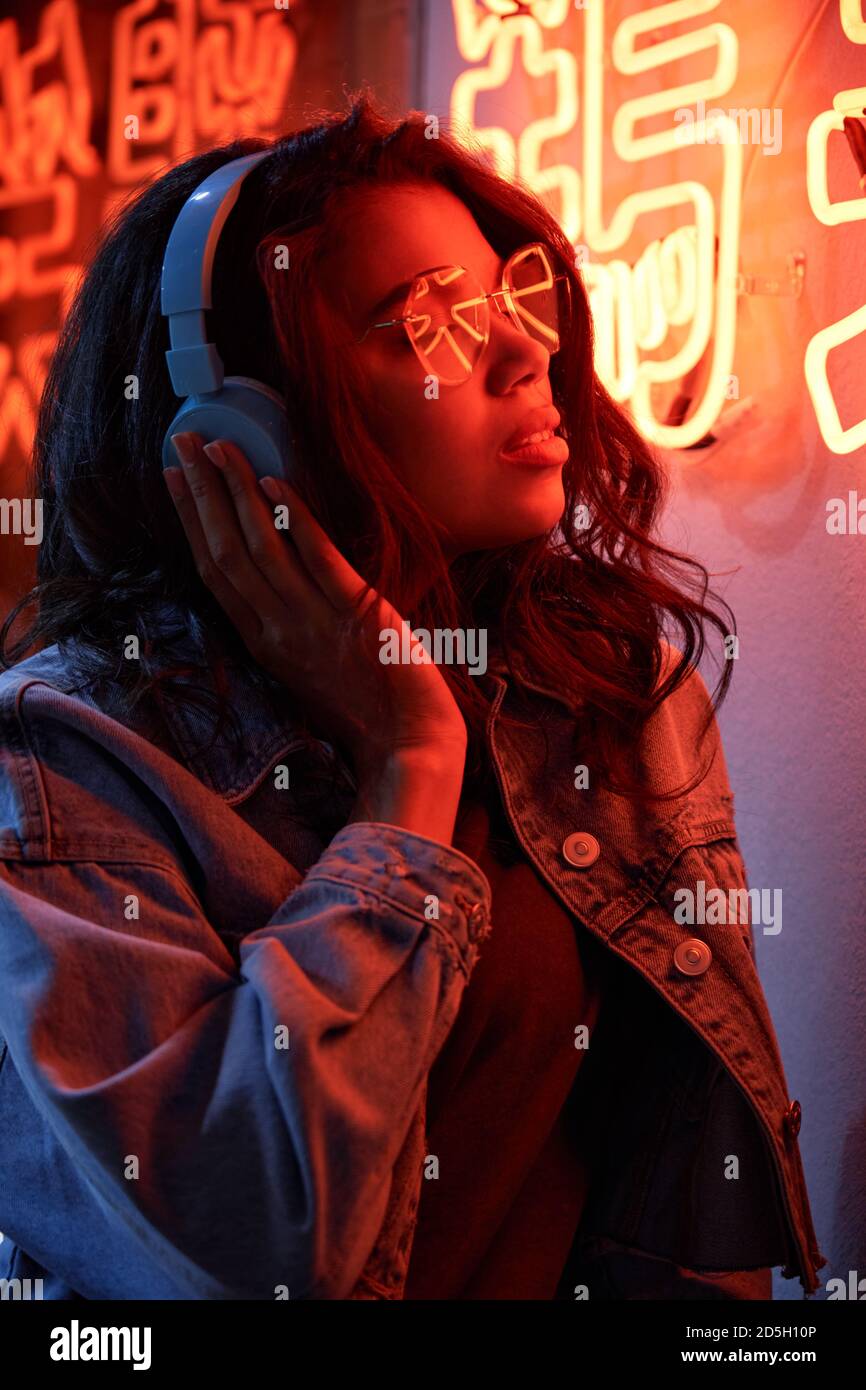 African American lady wearing headphones listening music in neon light. Stock Photo