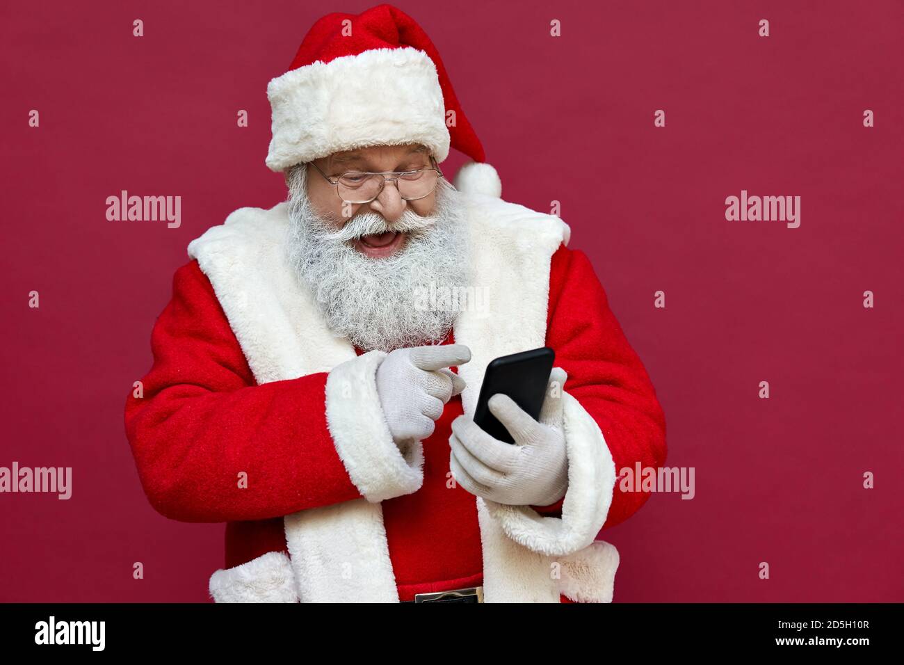 Happy excited Santa Claus using smart phone isolated on red background. Stock Photo