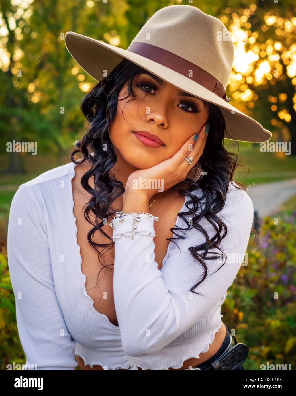 Young Latina woman is wearing a hat outdoors during sunset Stock Photo