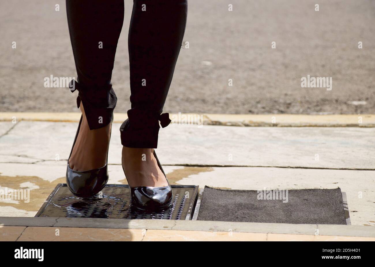 feet of a woman, wiping her shoes on a disinfectant mat before entering