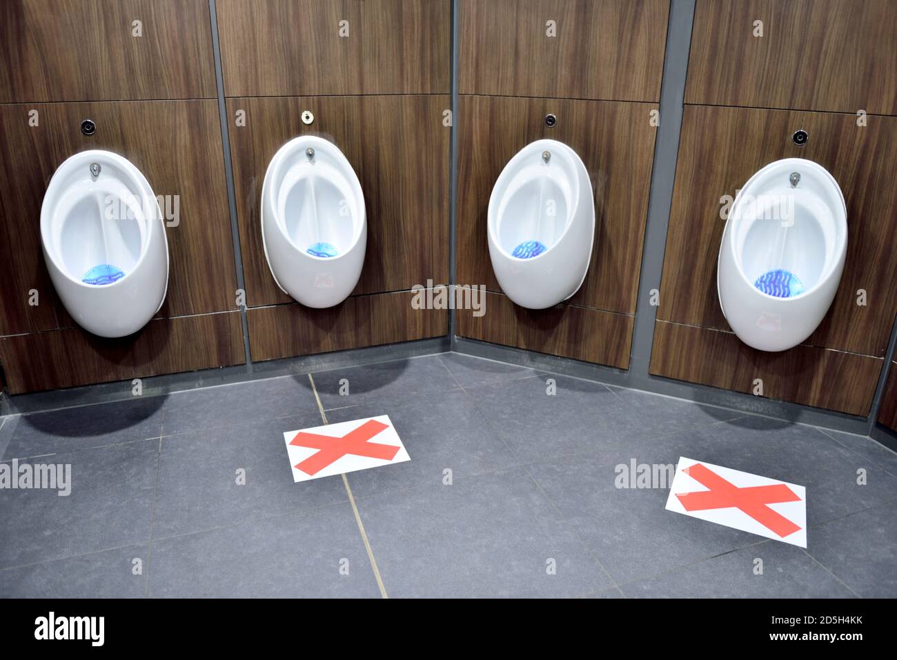 Urinals in public toilet with every other one marked not to be used due to Covid-19 and social distancing Stock Photo