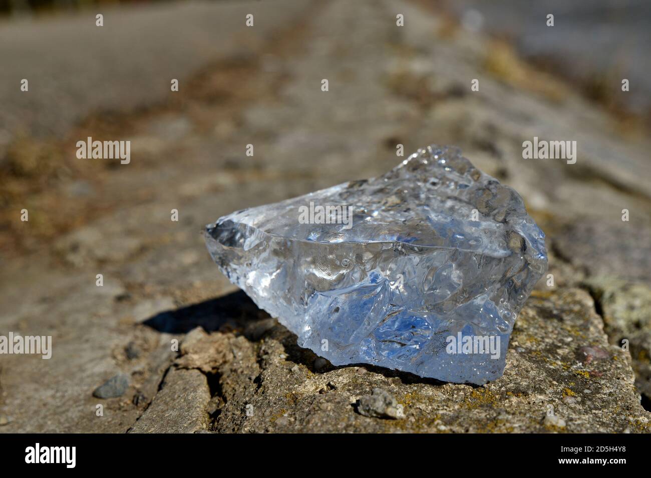 Fragment of ice from near. Transparent bluish ice on the ground. Stock Photo