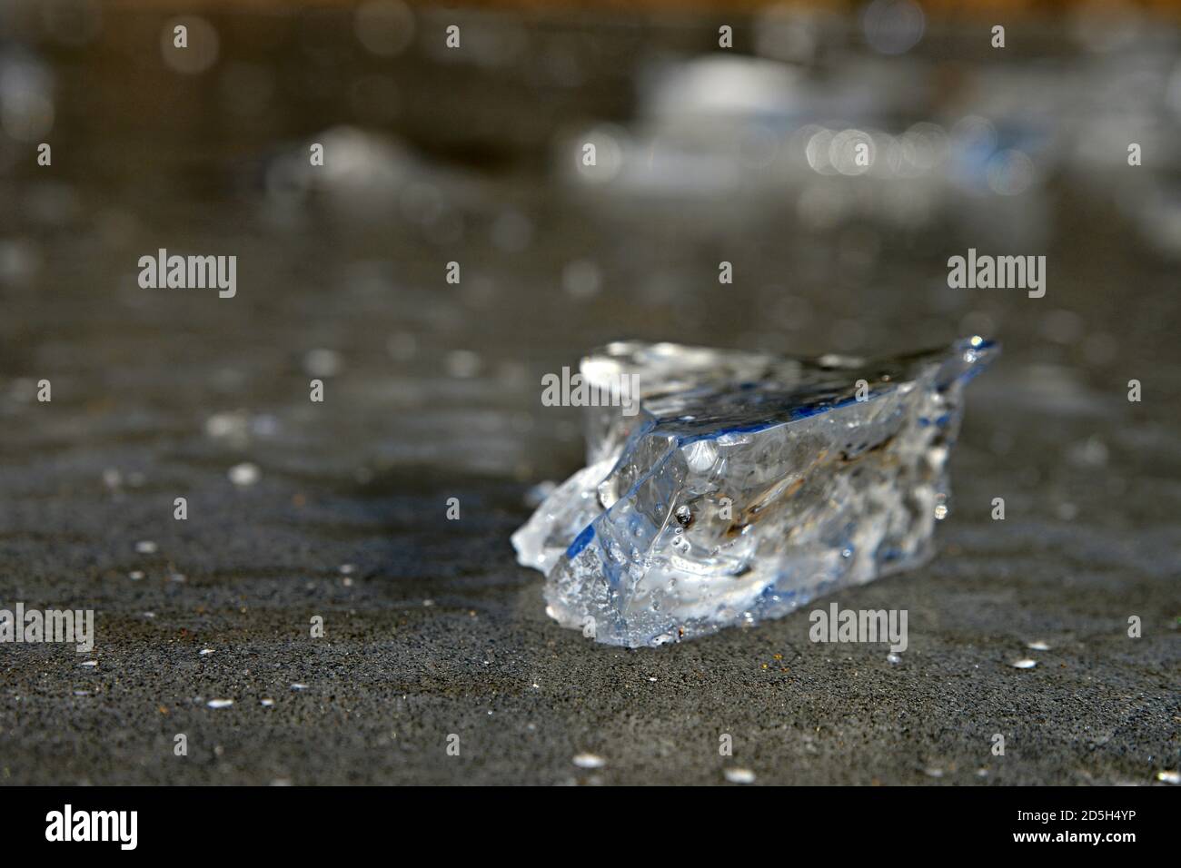 Fragment of ice from near. Transparent bluish ice on the ground. Stock Photo