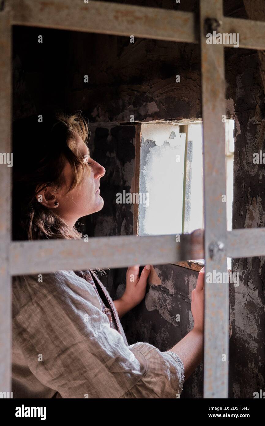 Woman in vintage clothes at window behind prison bars. Retro style costume on Halloween Stock Photo