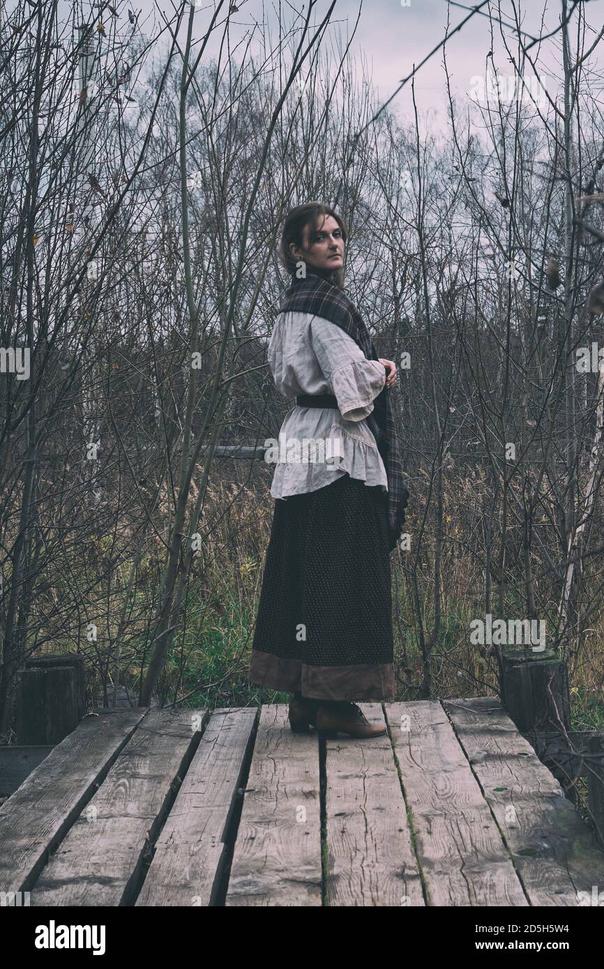 A woman in a headscarf looks from the bridge at the old pond. Girl in a ...
