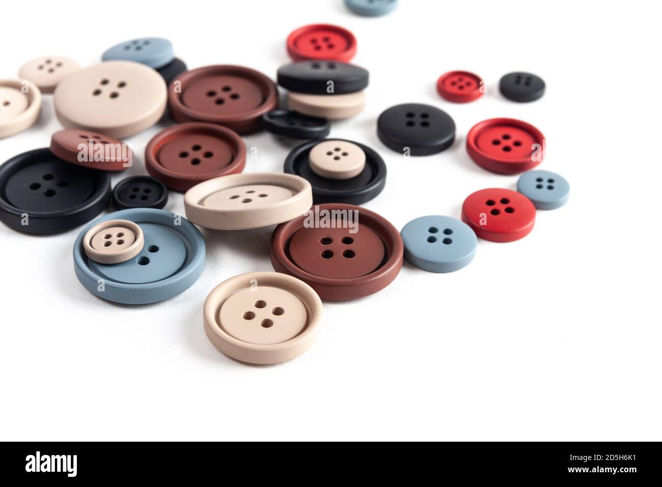Pile of color brown, beige, grey, red, black plastic matte buttons on white, beautiful needlework, minimalism. Use for sewing. Space for text. Stock Photo
