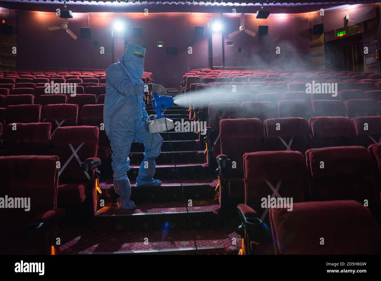 A worker wearing a personal protective suit PPE disinfecting the seats inside the 'Delite' movie theater.One of the oldest cinema halls located in Old Delhi prepares to reopen from 15th of October. Stock Photo