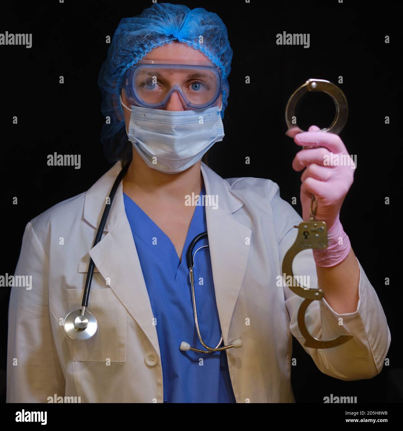 A doctor in a blue uniform with handcuffs on his hands, close-up. Medic in shackles, the concept of coronavirus quarantine in the world Stock Photo