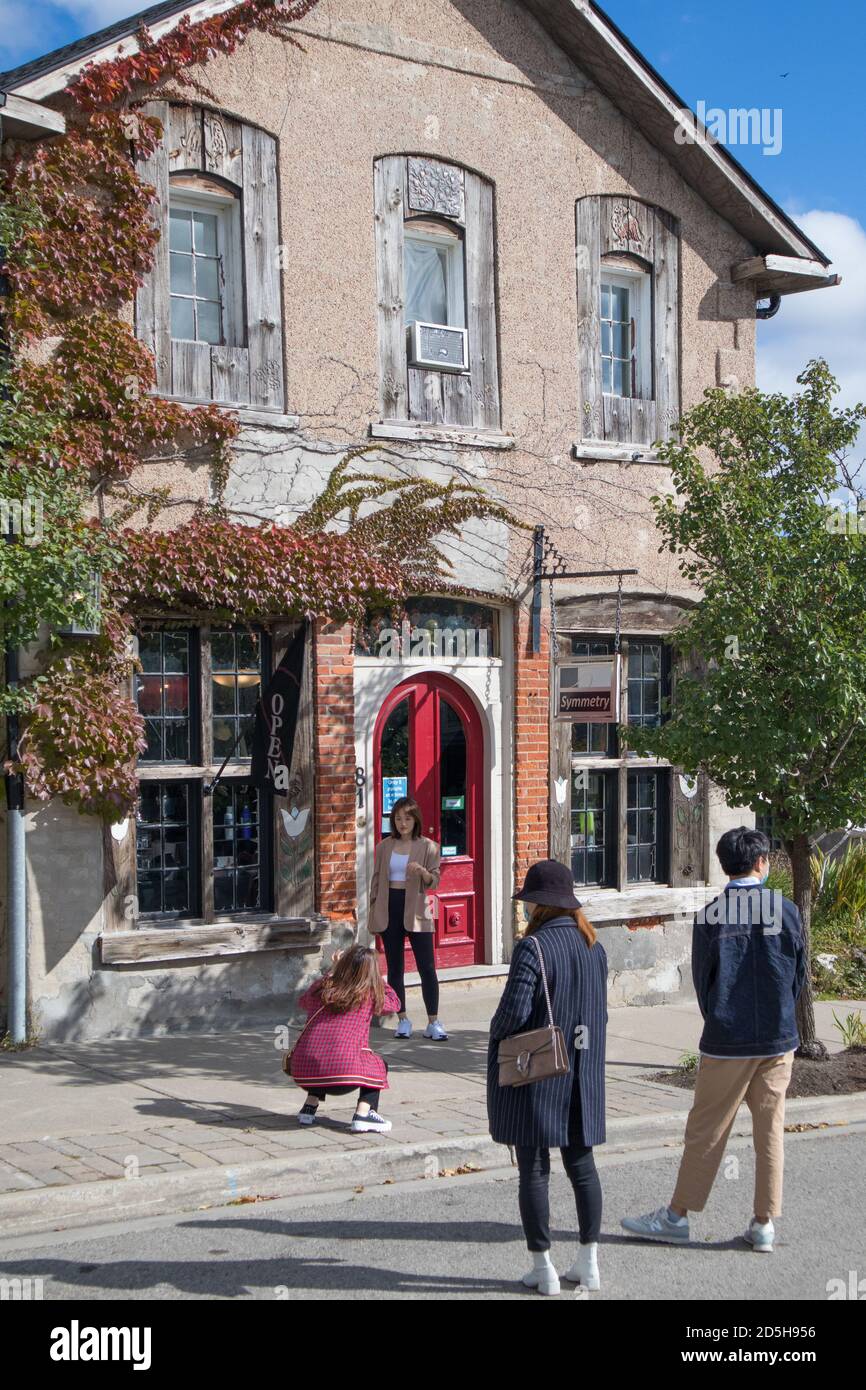 She takes pictures of her girl friend in Elora, in front of  the Symmetry shop. Some young Asians traveling together.. Stock Photo