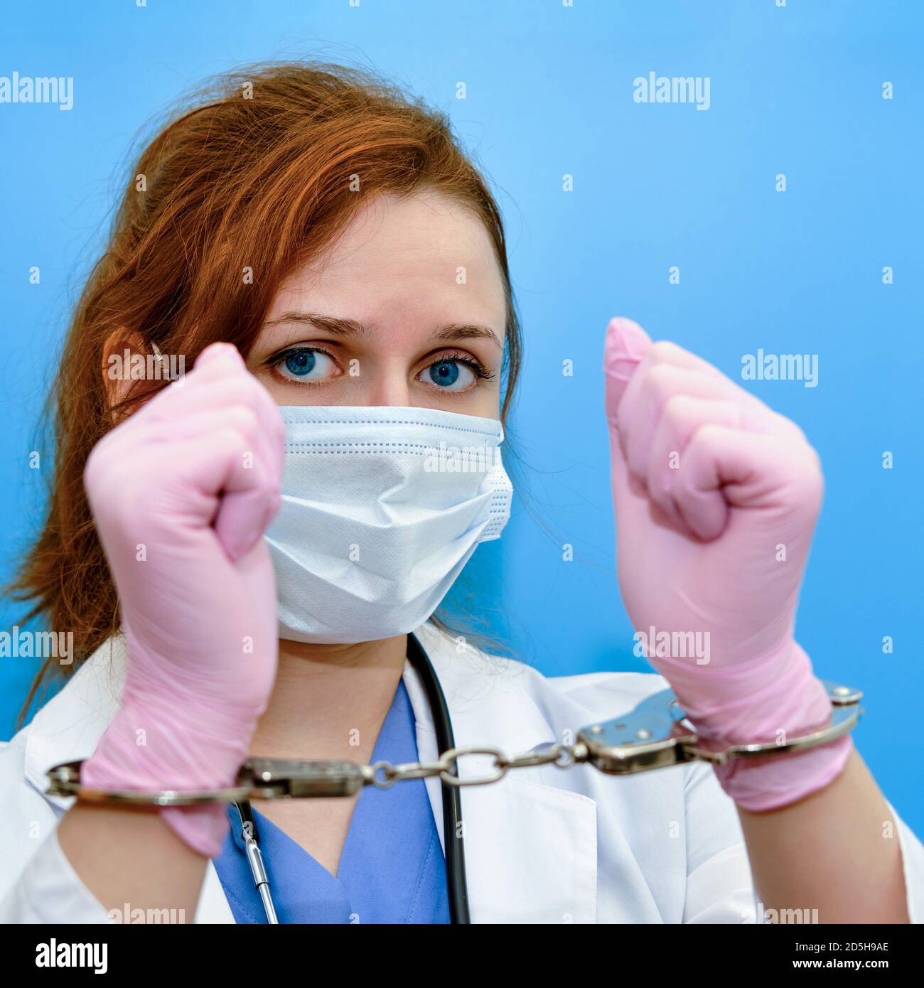 A doctor in a blue uniform with handcuffs on his hands, close-up. Medic in shackles, the concept of coronavirus quarantine in the world Stock Photo