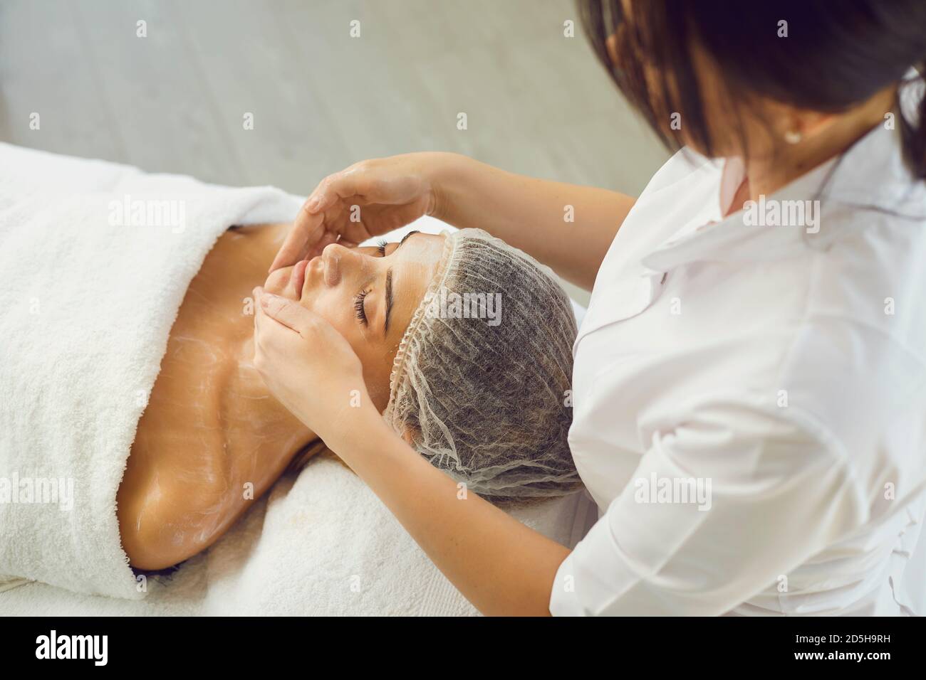 Cosmetologist applying moisturizing cream ro womans face and shoulders during skincare Stock Photo