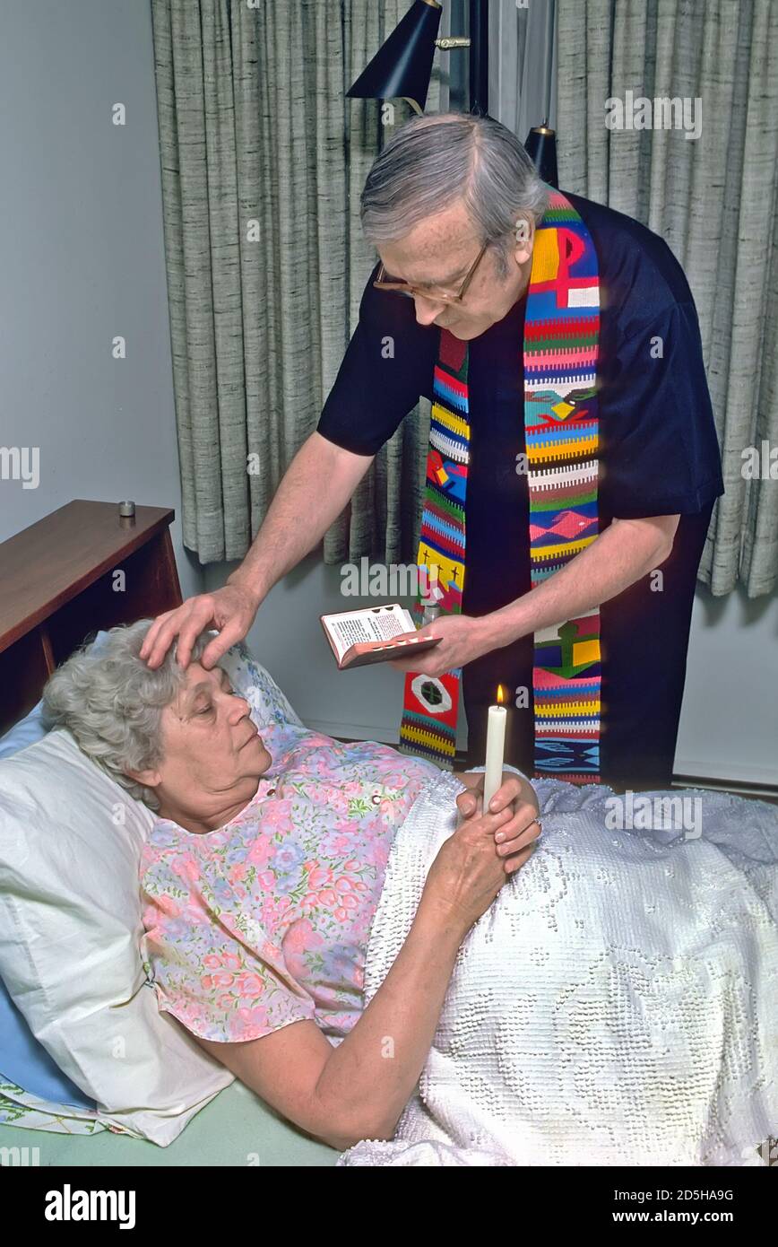 Catholic priest administers last rites to sick elderly female in bed The sacrament of Anointing of the Sick Stock Photo