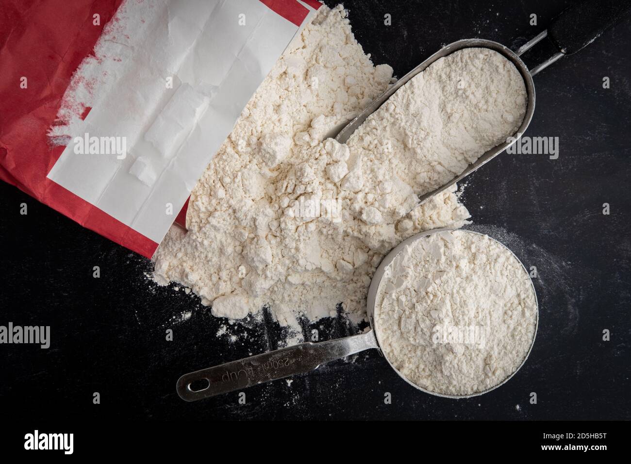 Bag of flour poured on the counter with a scoop and measuring cup Stock Photo