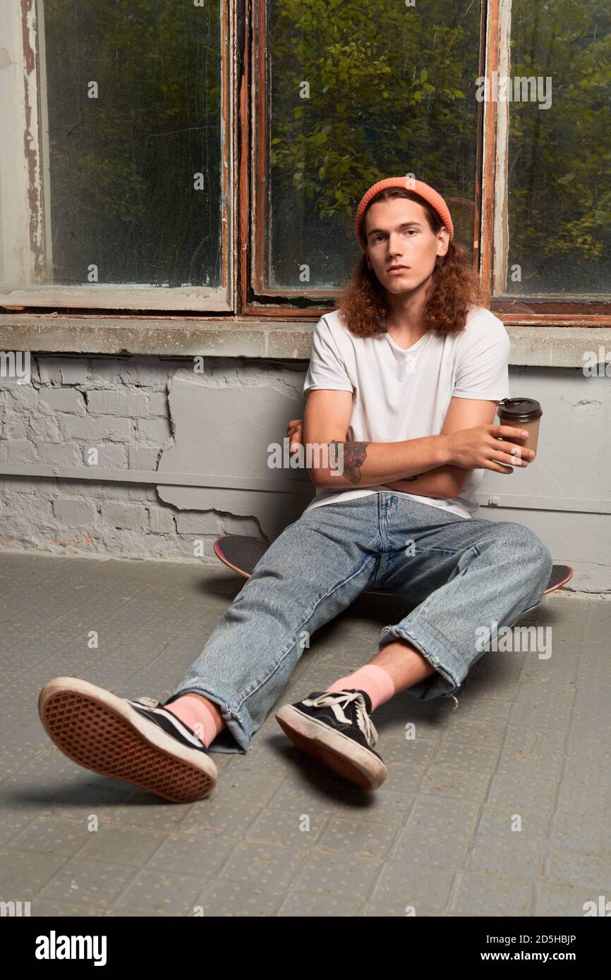 Young adult guy sitting on floor with beverage Stock Photo