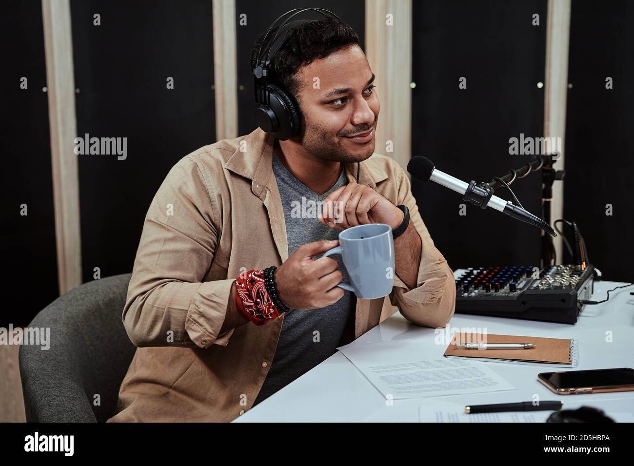 Portrait of young male radio host going live on air, talking with guest,  holding a cup of coffee or tea while sitting in studio Stock Photo - Alamy