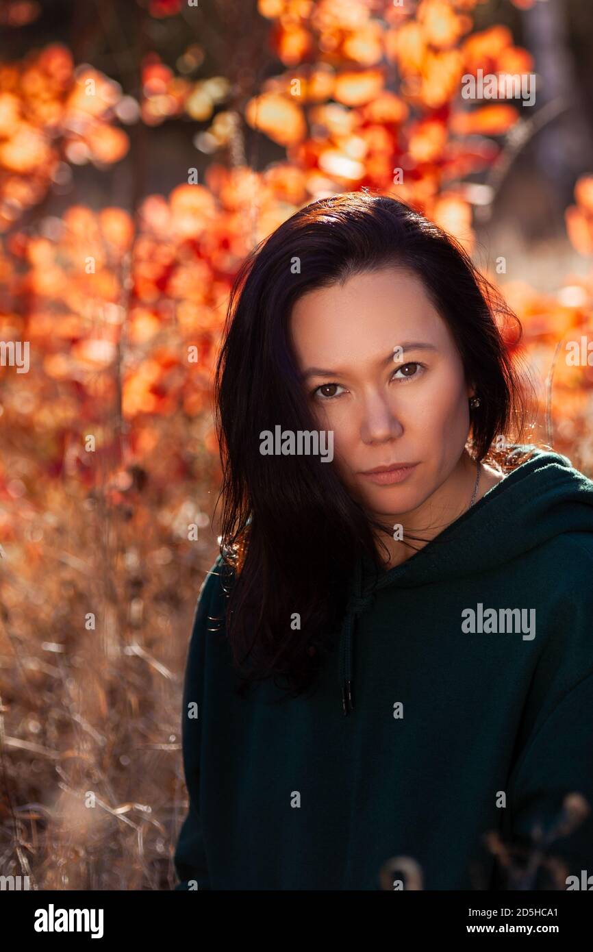 portrait of a beautiful Asian serious young woman in an autumn forest at sunset Stock Photo