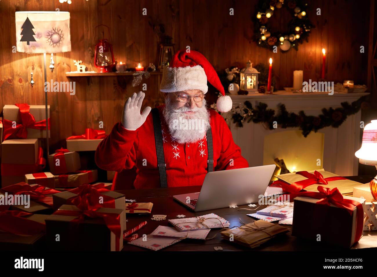 Happy Santa waving hand video calling child on laptop sitting at home table. Stock Photo
